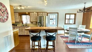 A modern kitchen with wooden cabinets, a central island, and two bar stools. - Orvis Outpost
 (Ridgway)