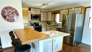A modern kitchen with wooden cabinets, stainless steel appliances, and a central island with stools. - Orvis Outpost
 (Ridgway)
