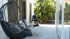 A patio with a hanging chair, a table, and a grill.
