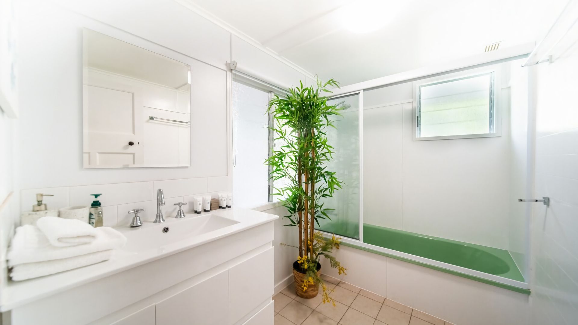 A bathroom with a white vanity, a large mirror, a bamboo plant, and a glass shower enclosure.