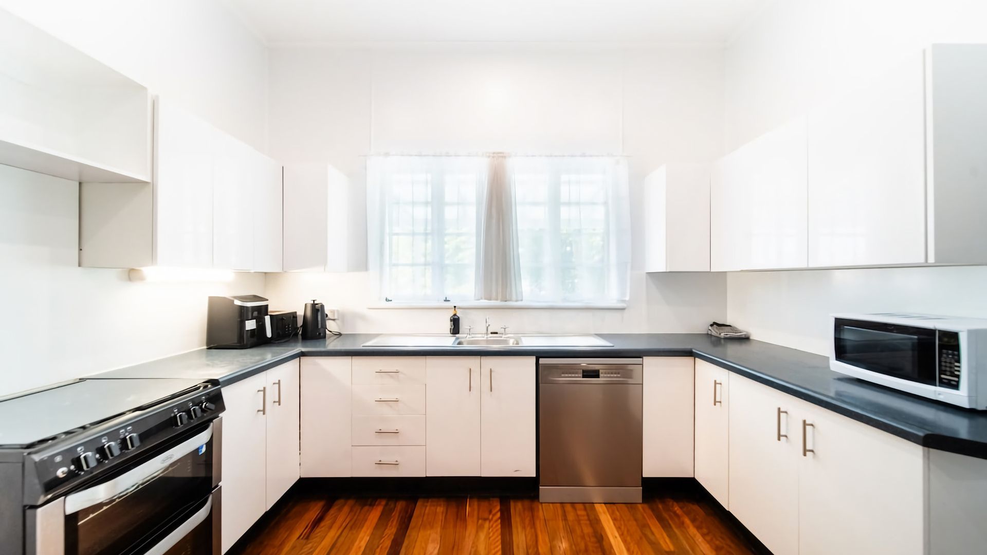 A modern kitchen with white cabinets, a black countertop, a stainless steel dishwasher, and a microwave.