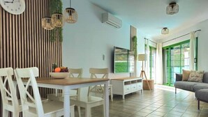 A modern living room with a dining area, a flat-screen TV, and a large window with green frames. - La Villa del Valle (CN)