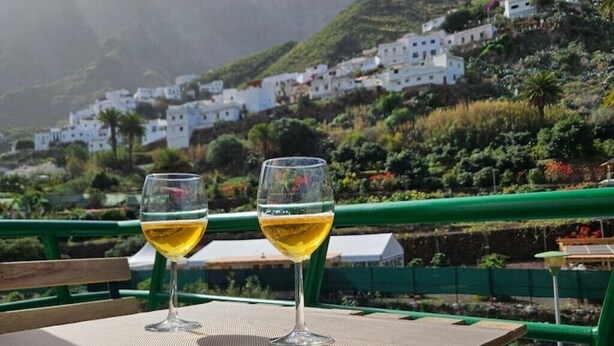 Two glasses of white wine on a table with a view of white buildings on a hillside. - La Villa del Valle (CN)