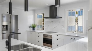 A modern kitchen with a stainless steel refrigerator, double sink, built-in oven, and a black range hood.