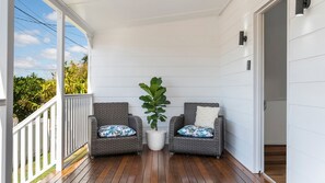A covered porch with two wicker chairs, a potted plant, and a view of the outdoors.