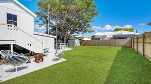 Un patio trasero con una casa blanca, una valla de madera y un césped.