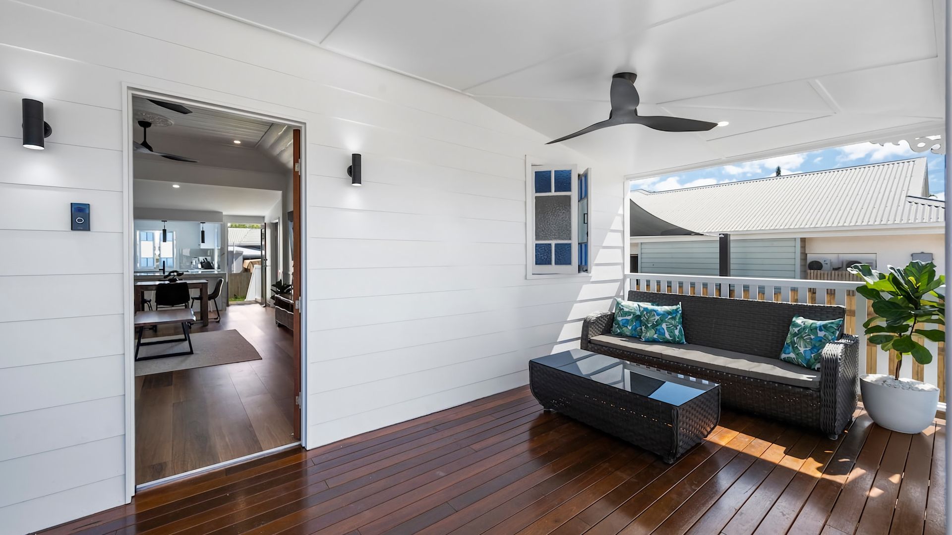Ein modernes Interieur mit Holzboden, einer Couch mit Kissen, einem Glastisch und einem Deckenventilator.