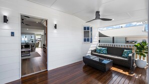 A modern interior with a wooden floor, a sofa with cushions, a glass coffee table, and a ceiling fan.