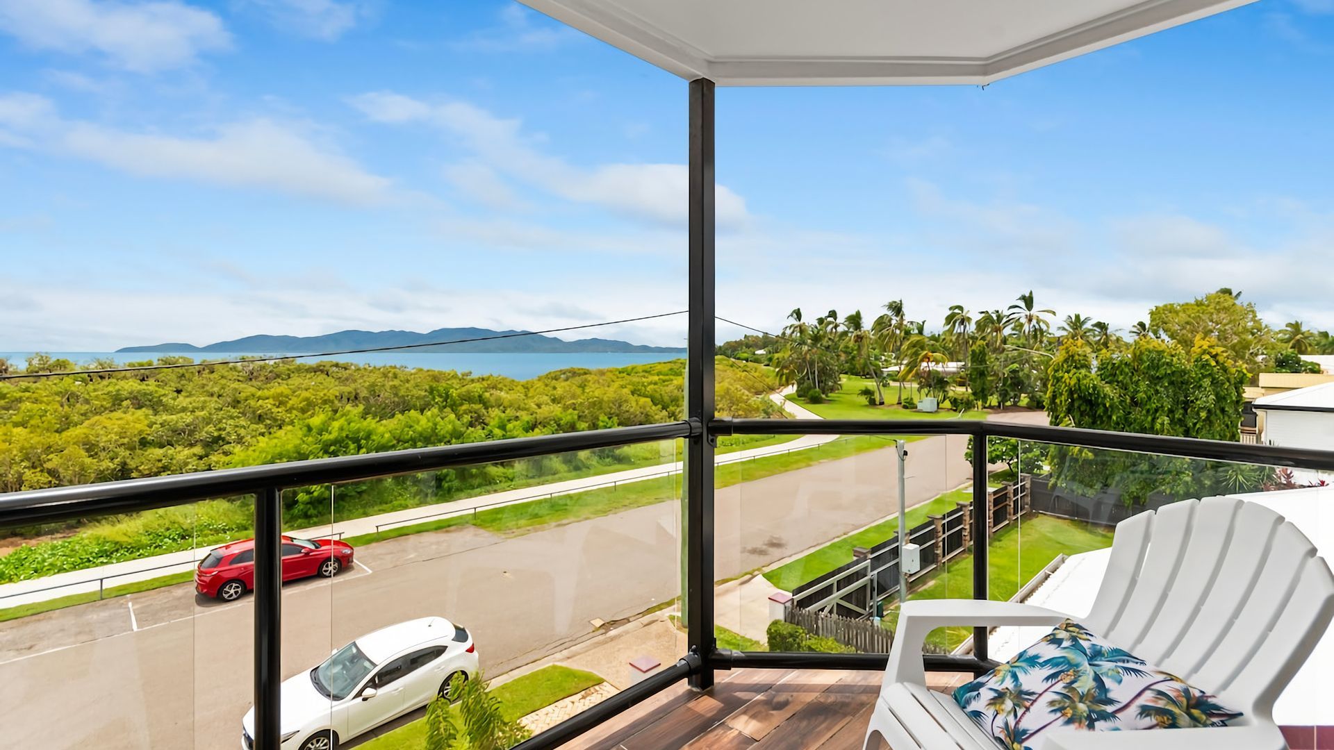 A balcony with a view of a road, cars, and greenery.