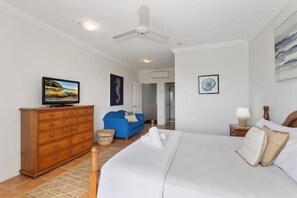 Een slaapkamer met een bed, een dressoir, een blauwe bank en een plafondventilator.
