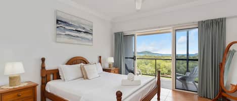 Hotelkamer met een bed, een plafondventilator, een schilderij, uitzicht door het raam en een balkon met een stoel.