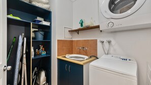 A compact laundry room with a washing machine, a drying machine, and a shelf with cleaning supplies.