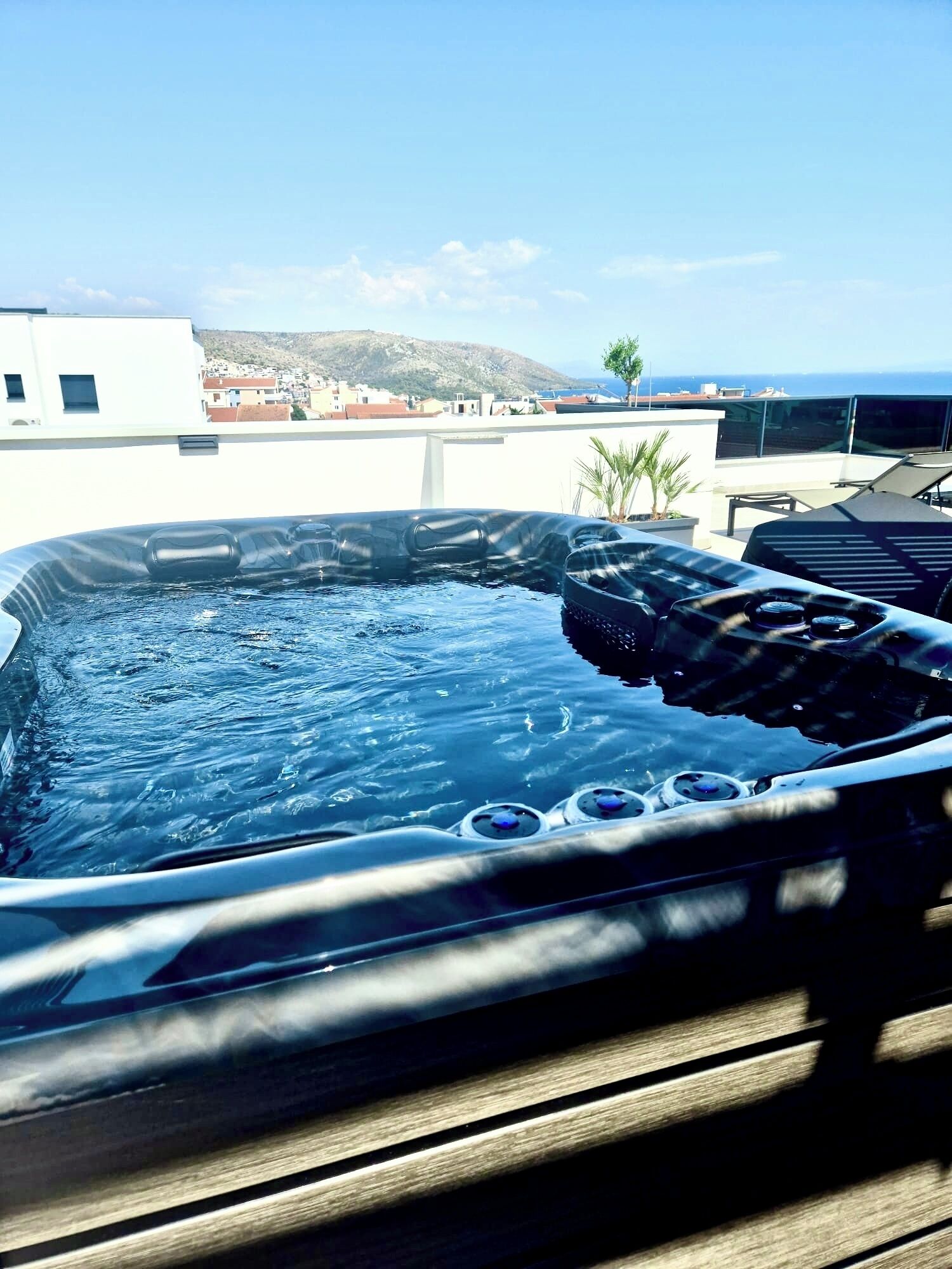 A hot tub on a rooftop with a view of the sea and buildings in the background.