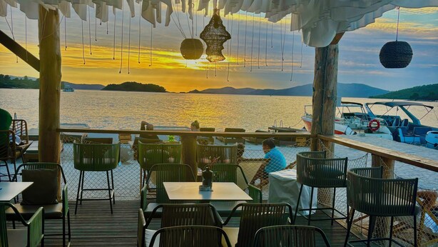Un restaurant doté d’une terrasse extérieure donnant sur un plan d’eau, avec une plateforme en bois et des chaises.