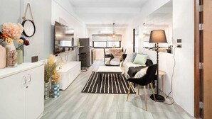 A modern living room with a sofa, a coffee table, and a TV. There is a kitchen area with a fridge and a microwave. - Roombix CityHouse -CozyHouse Chatuchak For 12 ppl - RB2 (Krung Thep Maha Nakhon)