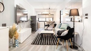 A modern living room with a sofa, a coffee table, and a rug. There is a TV mounted on the wall and a lamp on a side table. - Roombix CityHouse -CozyHouse Chatuchak For 12 ppl - RB2 (Krung Thep Maha Nakhon)