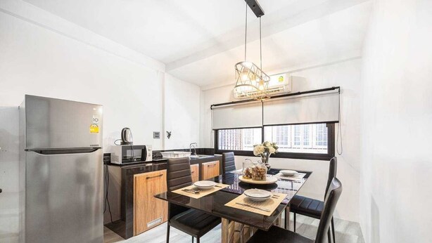 A compact kitchen with a refrigerator, microwave, and stove, a dining table with chairs, and a window providing natural light. - Roombix CityHouse -CozyHouse Chatuchak For 12 ppl - RB2 (Krung Thep Maha Nakhon)