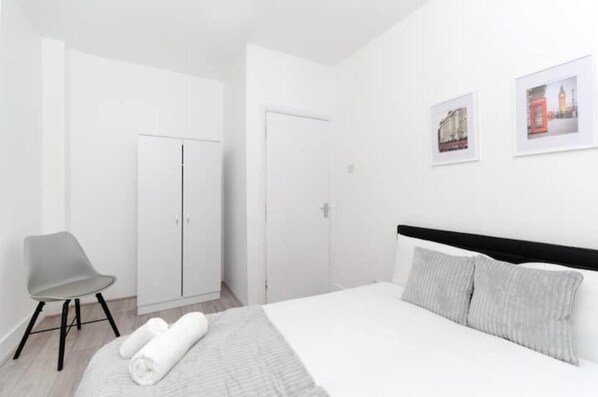 A bedroom with a bed, a chair, and two doors. - Flat 1 Covent Garden Apartments (London)