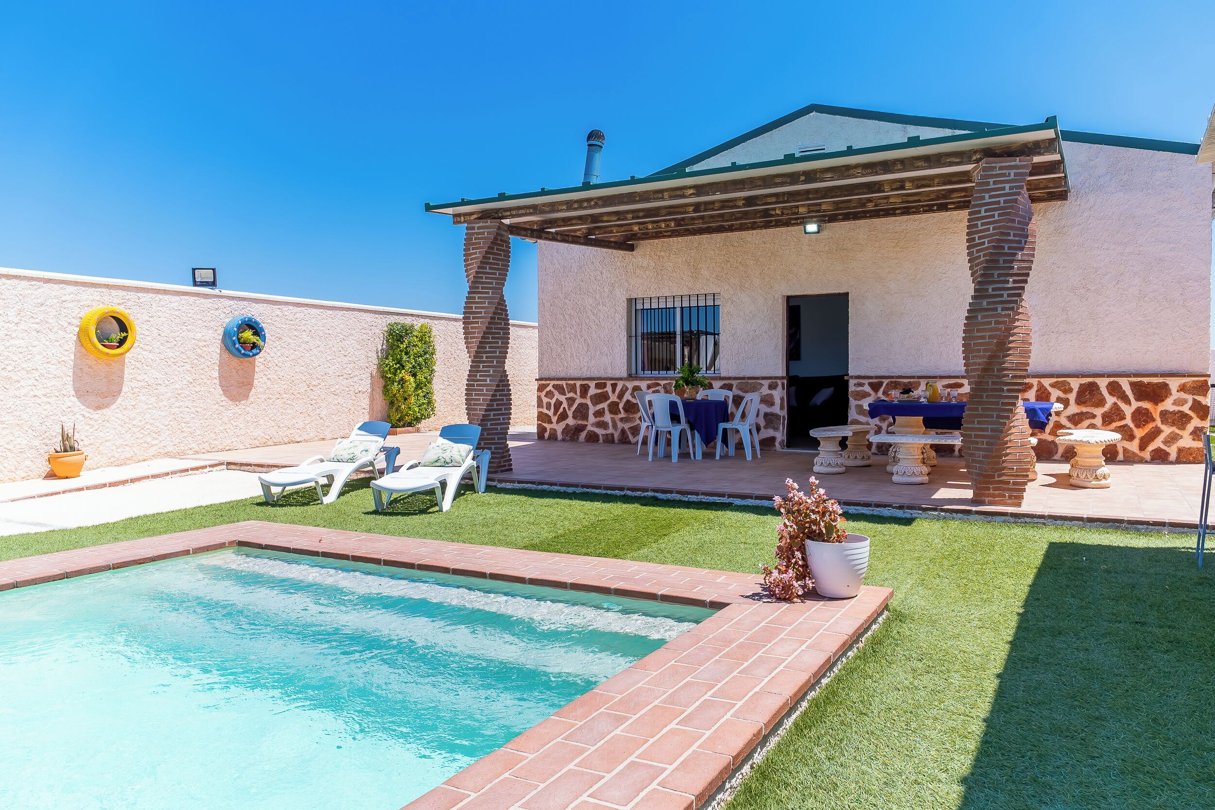 A pool with a patio area, a covered seating area, and a brick wall with decorative elements.