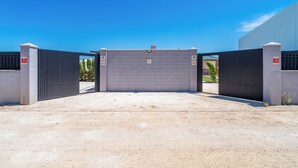 Una entrada con portón, cielo despejado arriba, camino de grava y un edificio moderno con techo plano.