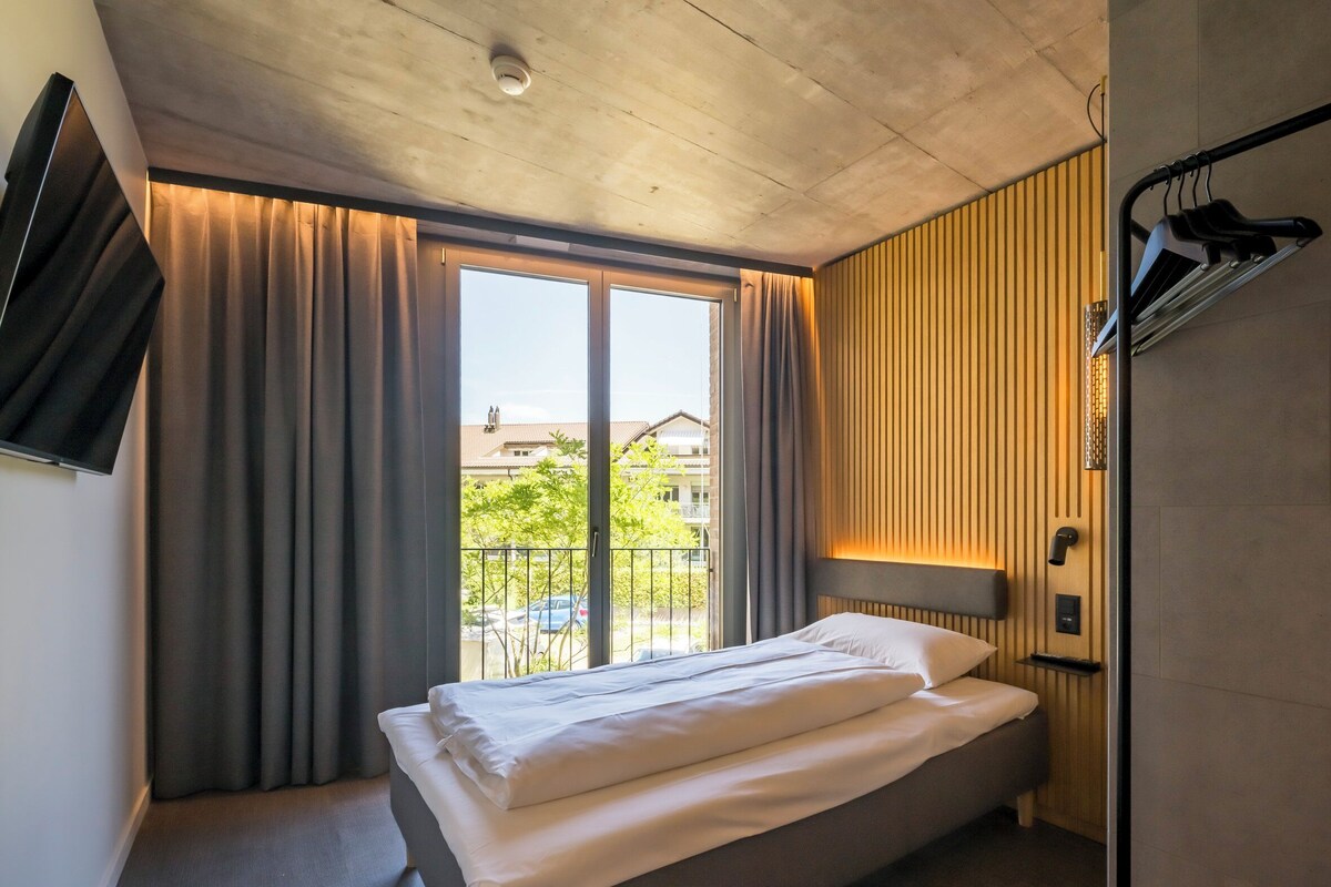 Una habitación de hotel moderna con una cama grande, un televisor montado en la pared y una ventana con cortinas.
