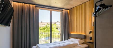 A modern hotel room with a large bed, a TV mounted on the wall, and a window with curtains.