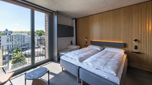 Habitació d'hotel moderna amb una finestra gran, un llit, una taula petita i una zona de seients.