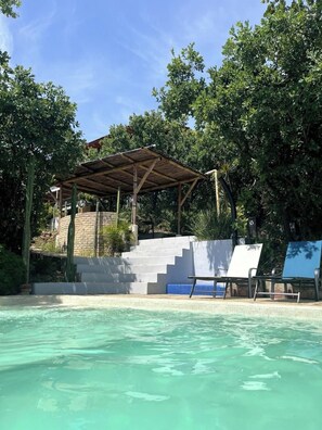 A swimming pool with a covered seating area and steps leading up to it.