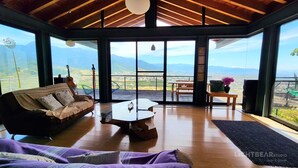 A spacious room with a large window offering a mountain view, a wooden ceiling, and a cozy seating area with a sofa and a coffee table.