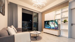 A modern living room with a sofa, a coffee table, a TV, and a sliding glass door leading to a balcony. - Happy Light Apartment in the Cardinal Court  (Ho Chi Minh City)