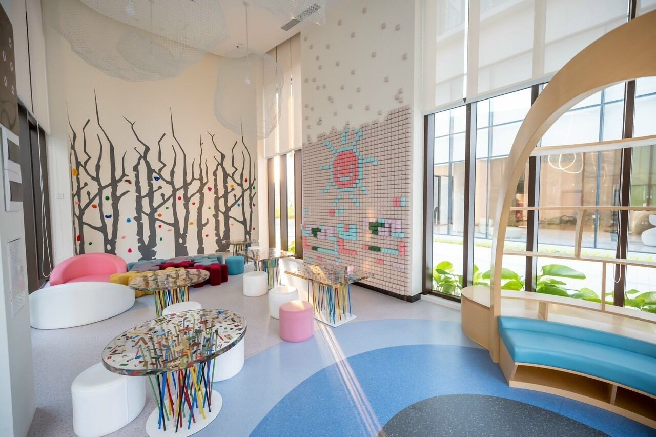 A modern, brightly lit indoor space with a large window, colorful wall art, and various seating options.