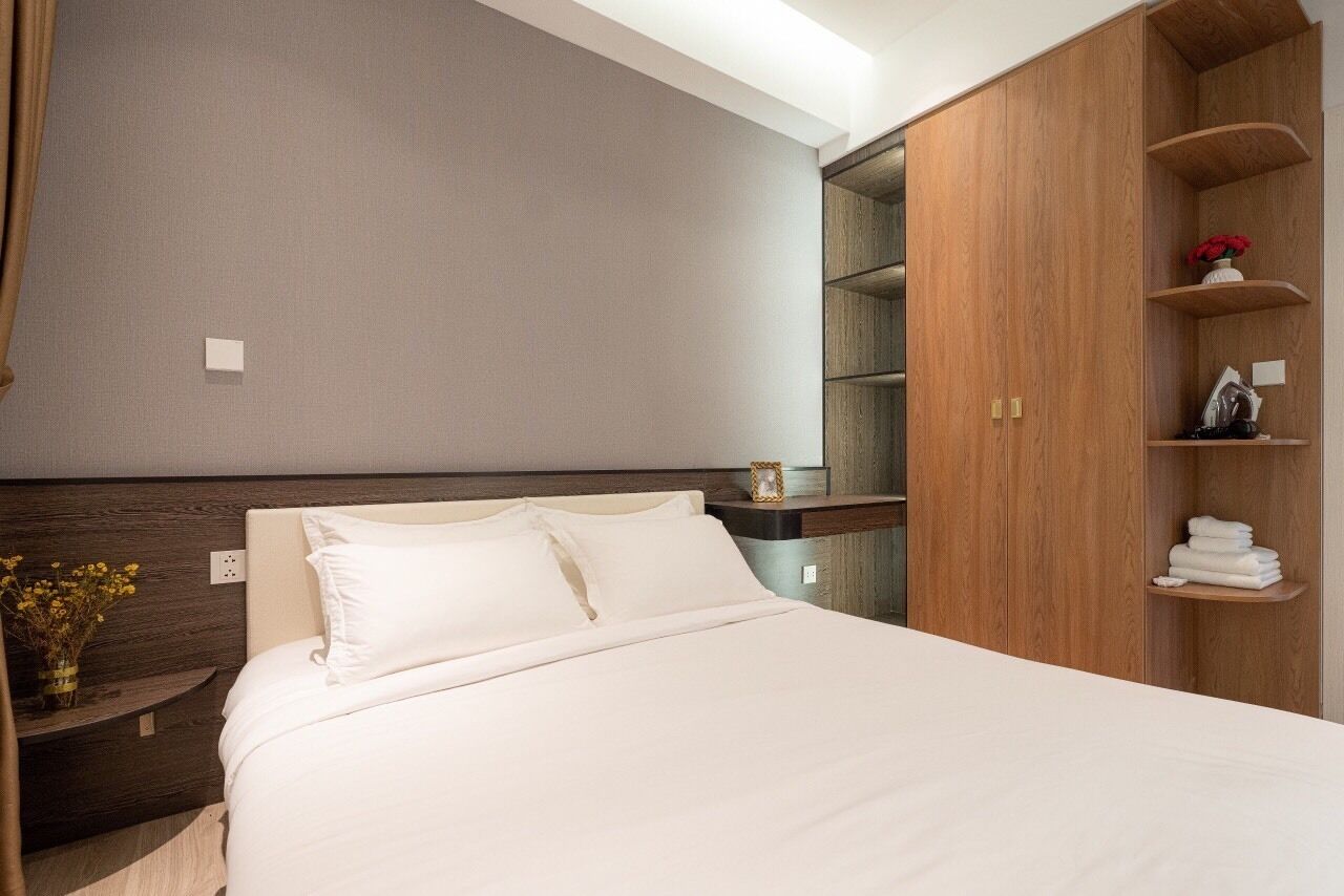 A bedroom with a bed, wooden wardrobe, and a nightstand with a vase of flowers.