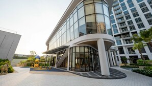 A modern building with a curved glass facade, a covered entrance, and a playground area. - Happy Light Apartment in the Cardinal Court  (Ho Chi Minh City)