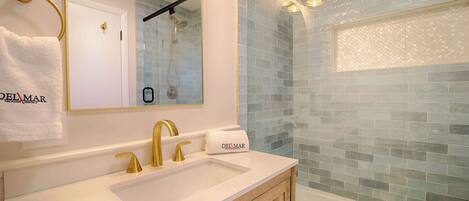 Un baño con lavamanos blanco, grifos dorados, un espejo y una ducha con mosaicos azules.