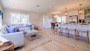 A spacious living area with a sofa, coffee table, and a kitchen with bar stools. - Water Views, Access to Grand Cove! (Dennis)