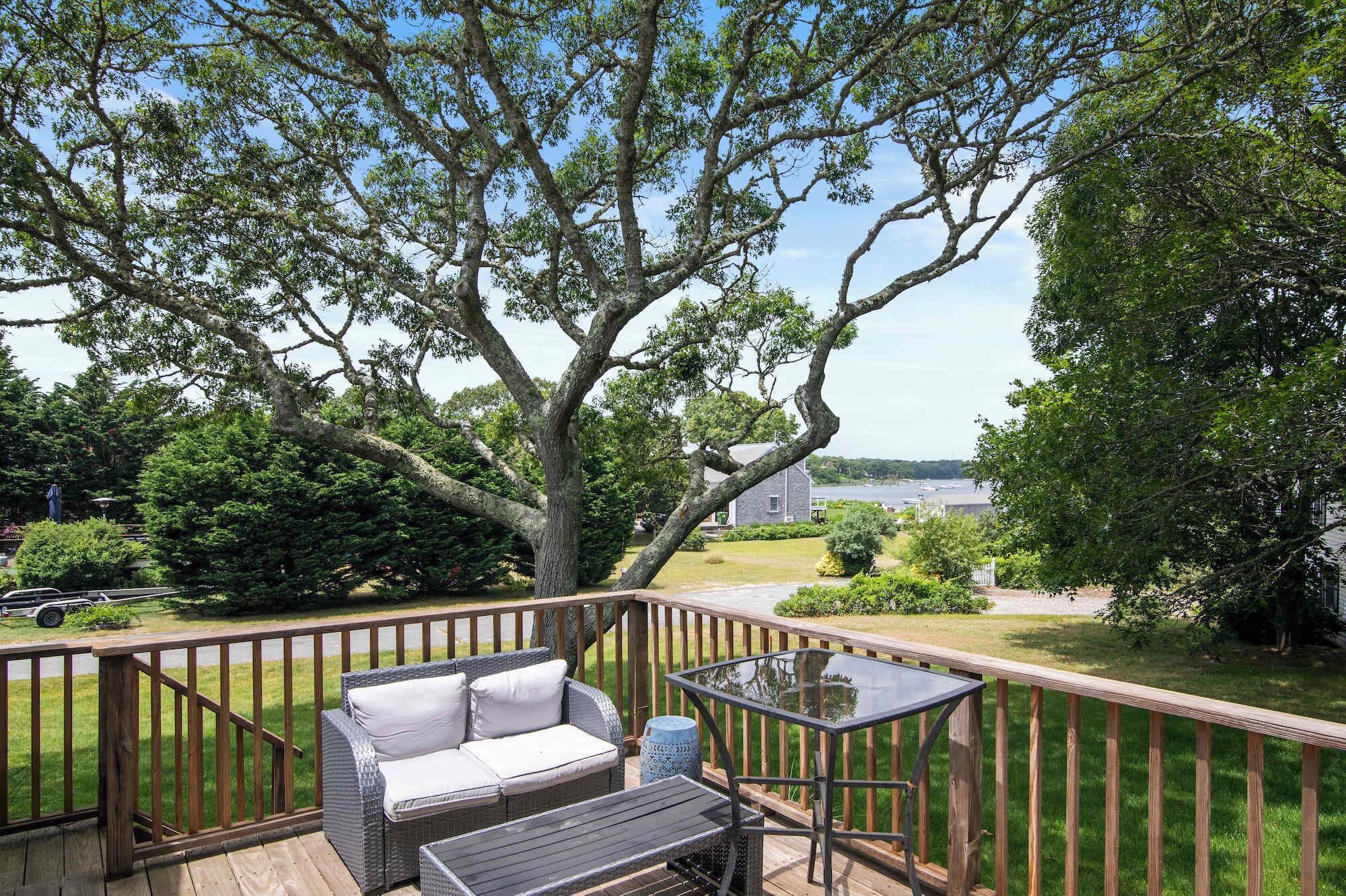Une terrasse dotée de mobilier d’extérieur, d’une table en verre et offrant une vue sur un lac et une maison.