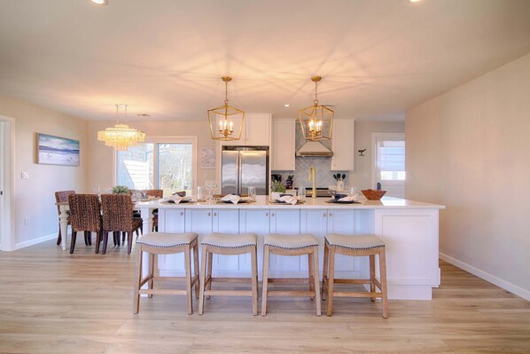 A kitchen with a central island, bar stools, pendant lights, and a dining area with chairs. - Water Views, Access to Grand Cove! (Dennis)