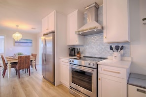 Een moderne keuken met witte kasten, roestvrijstalen apparatuur en een eethoek met een tafel en stoelen.