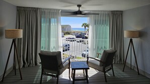 A hotel room with a balcony, two chairs, a table, and a ceiling fan.