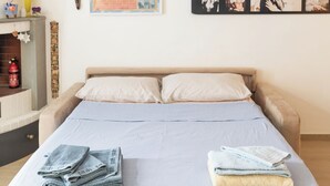 A bedroom with a bed, pillows, and folded towels. There is a poster on the wall and a small shelf with items. - Single-family home (Scandicci)