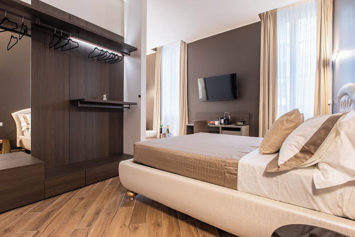 A modern hotel room with a large bed, a flat-screen TV, a desk with a chair, and a wardrobe with a hanging organizer.