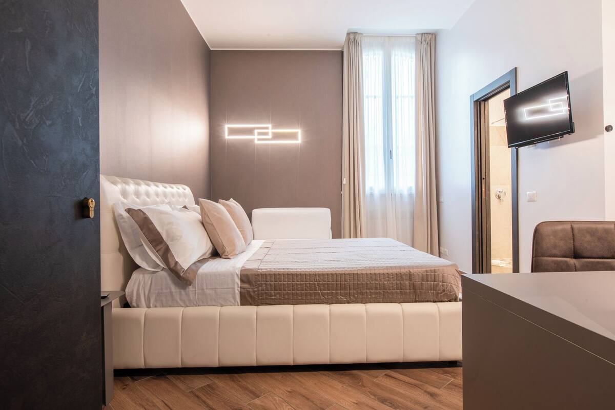 A modern bedroom with a large bed, a TV, and a view of the outdoors.