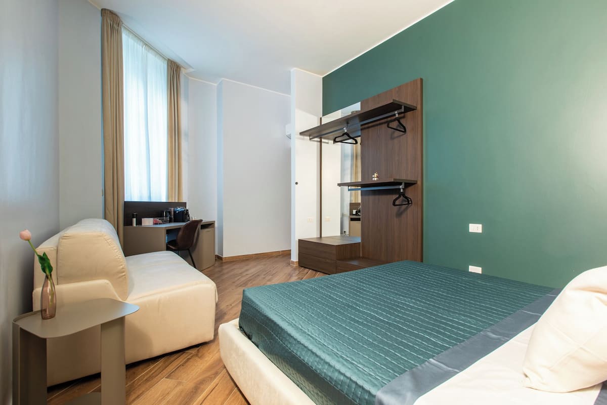 A hotel room with a bed, a desk, a chair, a wardrobe, and a mirror.