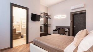 A modern hotel room with a bed, a desk, a chair, a TV, and a wardrobe. - The Dream Suites (Milan)