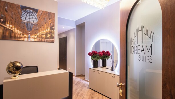 A hotel reception area with a modern design, a globe on the desk, a chandelier, a mirror with a floral arrangement, and a wall with a cityscape artwork. - The Dream Suites (Milan)