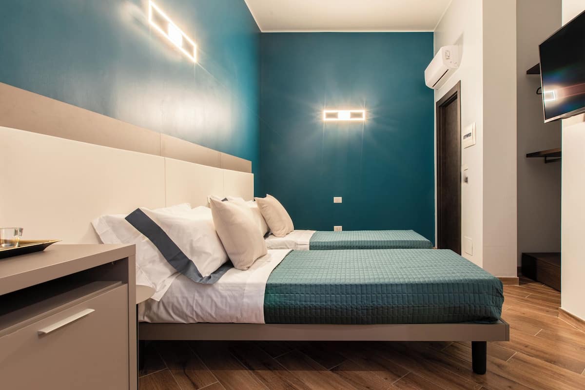 A modern hotel room with two beds, a wooden floor, and a TV on the wall.