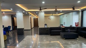 A modern lobby with a marble floor, black sofas, and ceiling fans. - The Grand Mansion Hotel (Greater Noida)