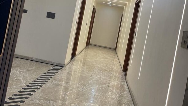 A modern hallway with a marble floor, recessed lighting, and wooden doors. - The Grand Mansion Hotel (Greater Noida)
