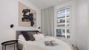 Un dormitorio moderno con cama, mesita de noche, ventana grande y vistas a la ciudad.