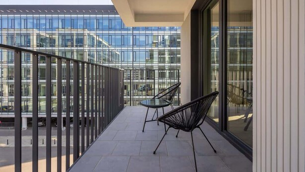 Un balcón con dos sillas, una mesa, amplios ventanales y vistas a un edificio moderno.